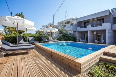 a pool with chairs and an umbrella on a wooden deck at Yianna Studios in Faliraki
