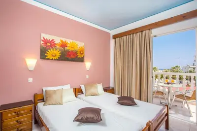 two beds in a room with a table and a balcony at Iatridis Studios Faliraki in Faliraki