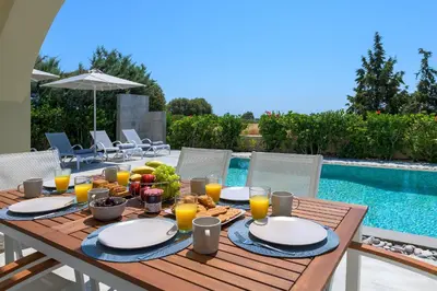 a wooden table with food and orange juice on it next to a pool at Olive Tree House in Gennadi