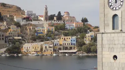a clock tower next to a body of water with houses at Odyssia in Symi