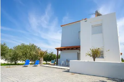 a white house with blue chairs in the courtyard at Alkion Villa in Gennadi