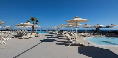 a group of chairs and umbrellas next to a swimming pool at Belair Beach Hotel in Ixia