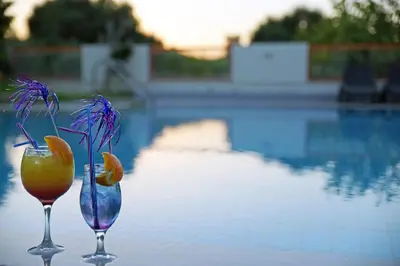 two wine glasses with a flower in them next to a pool at Falirala Central in Faliraki