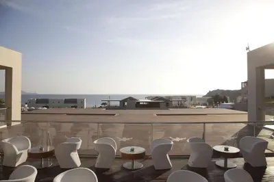 a room with white chairs and tables on a balcony at Port Royal Villas and Spa - Adults Only in Kolimbia