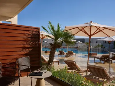 a patio with chairs and umbrellas and a pool at Port Royal Villas and Spa - Adults Only in Kolimbia