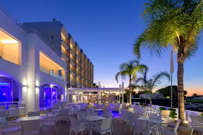a restaurant with white tables and chairs and palm trees at Oceanis Park Hotel in Ixia