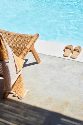 a wicker chair and pair of slippers next to a swimming pool at Mea Terra Villas in Lachania