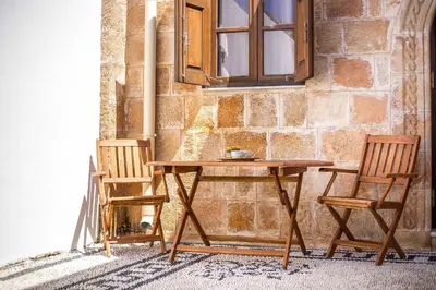 a wooden table and two chairs next to a stone wall at CasaLindos Festa in Líndos