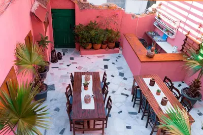 a patio with tables and chairs on a pink building at Mascot Garden Rooms in Rhodes Town