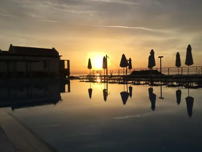 a pool of water with umbrellas and the sunset at LINDOS HORIZON in Líndos