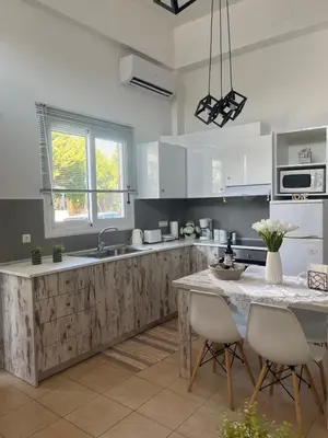 a kitchen with white cabinets and a table with chairs at La Casa de Tsampika in Koskinou