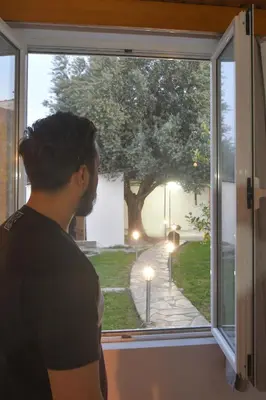 a man looking out a window at a tree at The Olive Garden House in Haraki