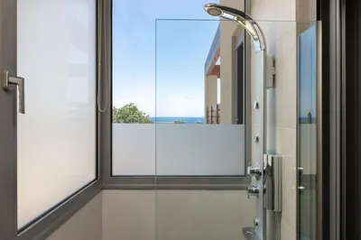 a bathroom with a glass shower with a window at Terpsis Pool Villa in Rhodes Town