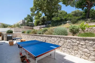 a ping pong table on a patio with a stone wall at Terpsis Pool Villa in Rhodes Town