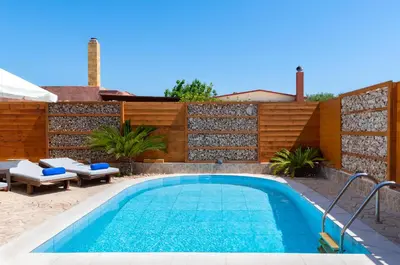 a swimming pool in a backyard with a wooden fence at Ifigeneia Villa in Afantou