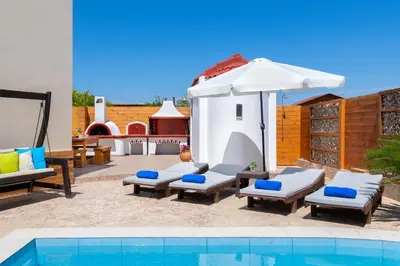 a patio with chairs and an umbrella and a pool at Ifigeneia Villa in Afantou
