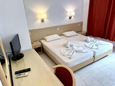 a room with two beds and a desk with a television at Savoy City Hotel in Rhodes Town