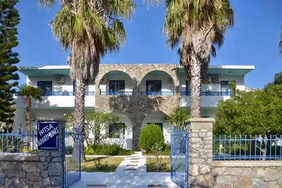 a building with palm trees in front of a fence at Nitsa's Apartments in Megálon Choríon