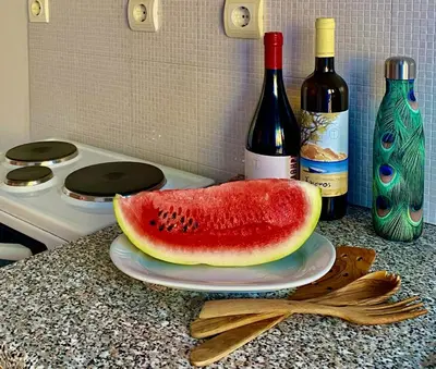 a slice of watermelon on a plate on a counter with wine bottles at Nitsa's Apartments in Megálon Choríon