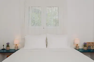 a bedroom with a white bed with two windows at Anatoli Traditional Villa in Archangelos
