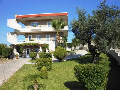 a large white building with trees and bushes at Villa Olive Grove in Afantou