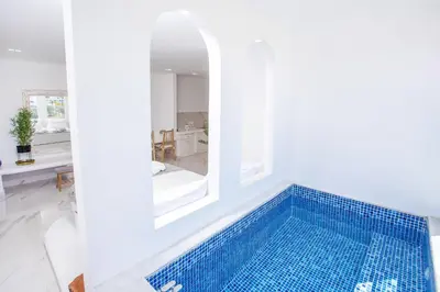 a swimming pool in a white room with a blue tile tub at Ammos Luxury Suites in Faliraki