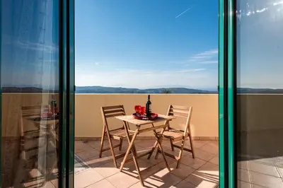a table with chairs and a bottle of wine on a balcony at Anemos Villa in Sálakos
