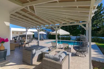 a patio with chairs and umbrellas next to a pool at Casa Bianca Villa in Kolimbia