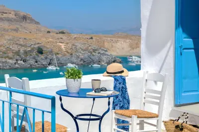 a woman sitting at a table on a balcony looking at the water at Lindos Beach Boutique Villa in Líndos