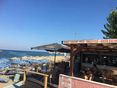 a beach with blue and white umbrellas and the ocean at RHODIAN TREASJURE Spiridione Studios in Faliraki