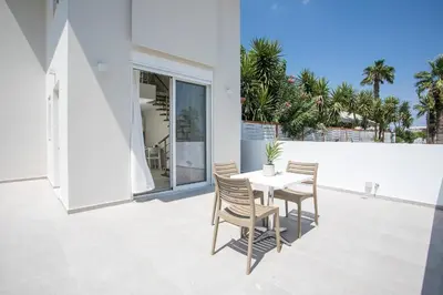 a white patio with a white table and chairs at Avi Suites Faliraki in Faliraki