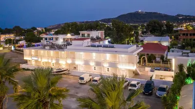 a large white building with cars parked in a parking lot at Avi Suites Faliraki in Faliraki