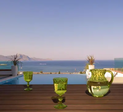 two green glasses and a vase on a wooden table at Luxury Villa Eos in vlicha