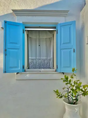 a window with blue shutters and a potted plant at Aetheria traditional house in Koskinou