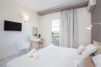 a white hotel room with two beds and a desk at Evita in Faliraki