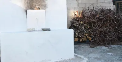 a white pillar with a rock on it next to a pile of wood at George's Studios in Archangelos