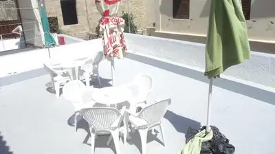 a patio with white tables and chairs and a green umbrella at Stavros Pension in Rhodes Town