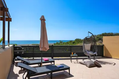 a patio with chairs and an umbrella and the ocean at Mare Blu 2 on the beach in Gennadi