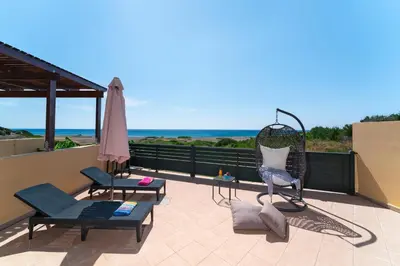 a patio with chairs and an umbrella and the ocean at Mare Blu 2 on the beach in Gennadi