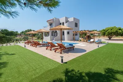 a pool with chairs and umbrellas in front of a house at Sun's Reach Villa in Rhodes Town