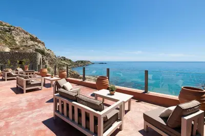 a patio with chairs and tables and the ocean at Stone Luxury Suites - Adults Only in Archangelos