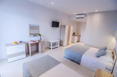 a white bedroom with a bed and a desk at Galazio Beach in Faliraki