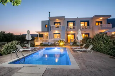 a villa with a swimming pool in front of a house at RITA MARE seafront villas heated Pools in Gennadi