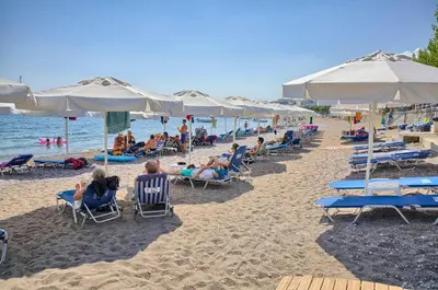 a group of people sitting on a beach with umbrellas at Haraki Bay Hotel and Luxury Apartments in Haraki