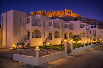 a white building with a mountain in the background at Haraki Bay Hotel and Luxury Apartments in Haraki