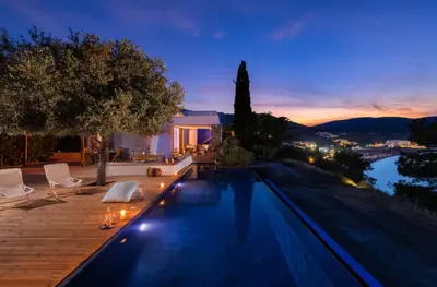 a swimming pool in front of a house at night at lindos kerylos villa in Líndos