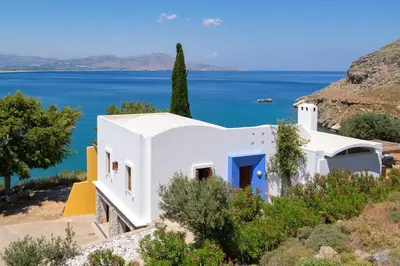 a white house with the ocean in the background at lindos kerylos villa in Líndos