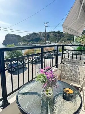 a glass table with a vase of flowers on a balcony at Orfeas Sea View House in Archangelos