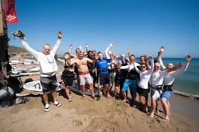 a group of people standing on the beach with their arms in the air at Prasonisi Club in Kattavía