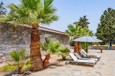 a group of chairs and an umbrella and palm trees at Madia Villa in Kolimbia
